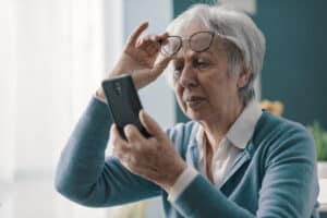 Older woman squinting and struggling to see her phone screen due to cataracts