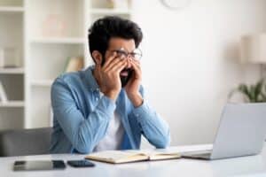 Man rubbing his eyes in front of a laptop due to digital eye strain that could be masking other serious conditions