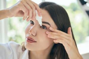 Woman putting in eye drops to relieve her chronic dry eye symptoms, possibly having a corneal surface disorder
