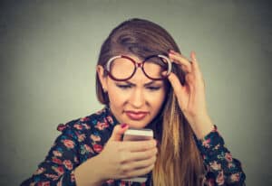 Young woman squinting while looking at her phone, struggling with blurry vision