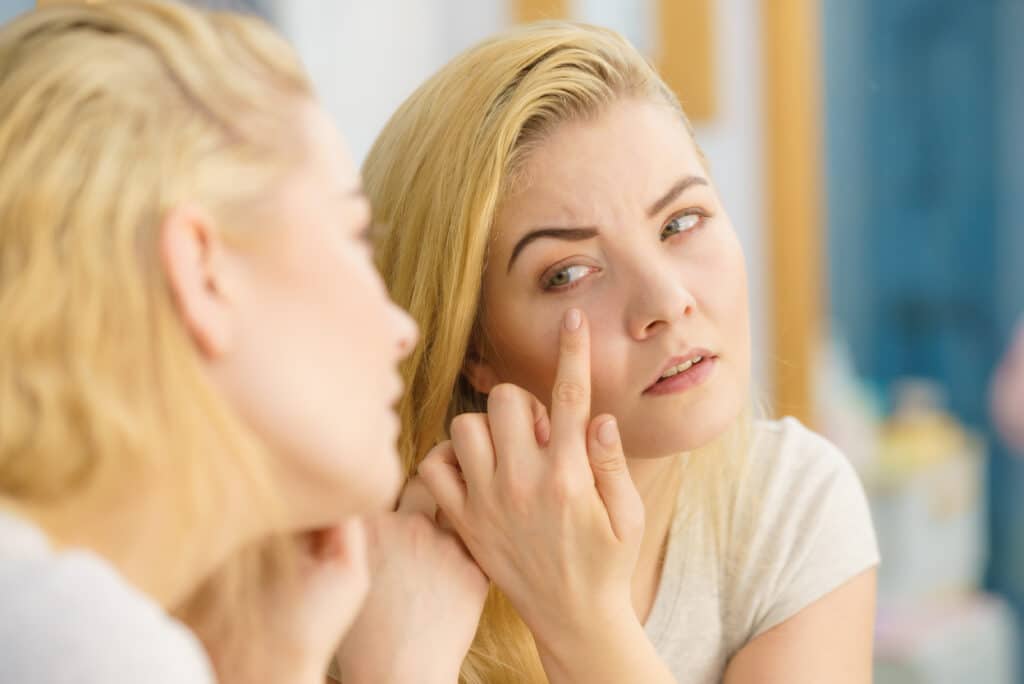 Woman looking at her skin in mirror Eyelid Papilloma Treatment Dallas TX
