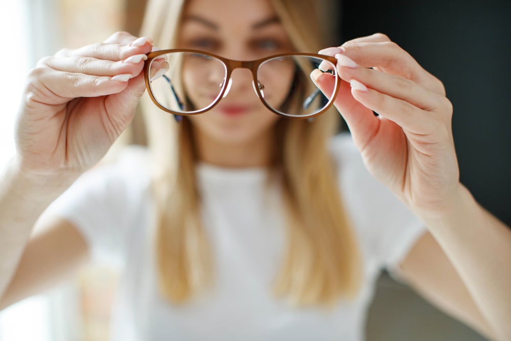 A woman holding her glasses away from her face to show how her vision has been corrected with LASIK. A woman holding her glasses away from her face to show how her vision has been corrected with LASIK.