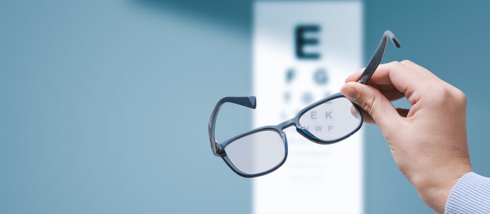 Close up of a patient holding up a pair of glasses in an eye exam room, clearly struggling with blurry vision. Close up of a patient holding up a pair of glasses in an eye exam room, clearly struggling with blurry vision.