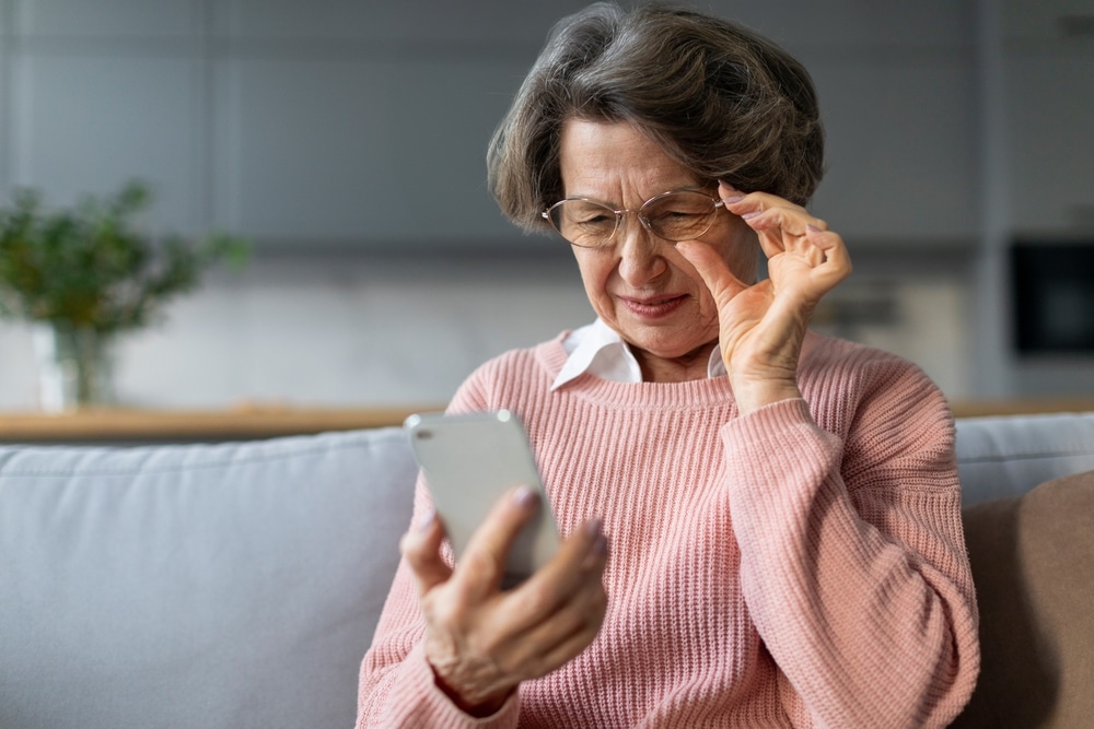 Older woman squinting while trying to read her phone, struggling due to cataracts